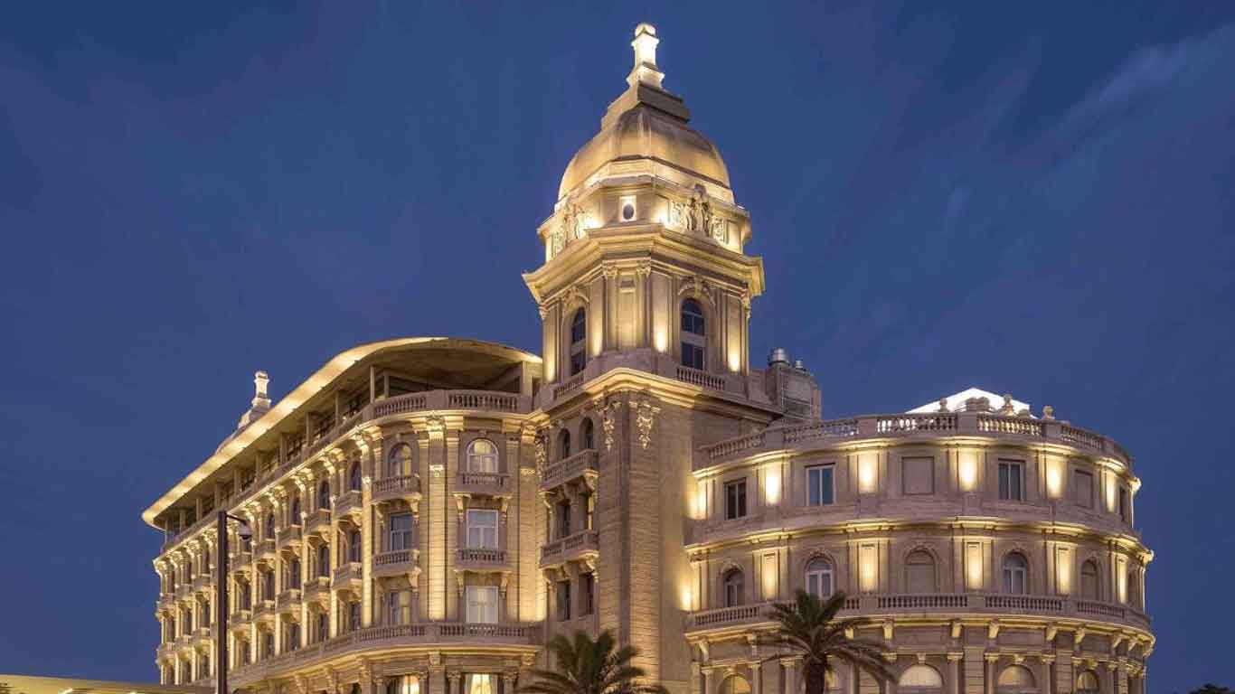 A imagem mostra o Sofitel Montevideo Casino Carrasco & Spa iluminado à noite. Este hotel luxuoso destaca-se pela sua arquitetura elegante e clássica, com detalhes iluminados que realçam suas linhas sofisticadas contra o céu noturno.
