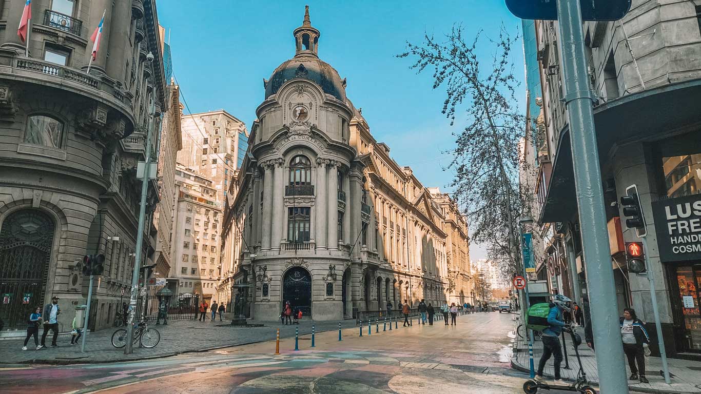 Vista de uma esquina movimentada no centro de Santiago, a região mais popular para se hospedar, destacando a arquitetura histórica e as ruas vibrantes.
