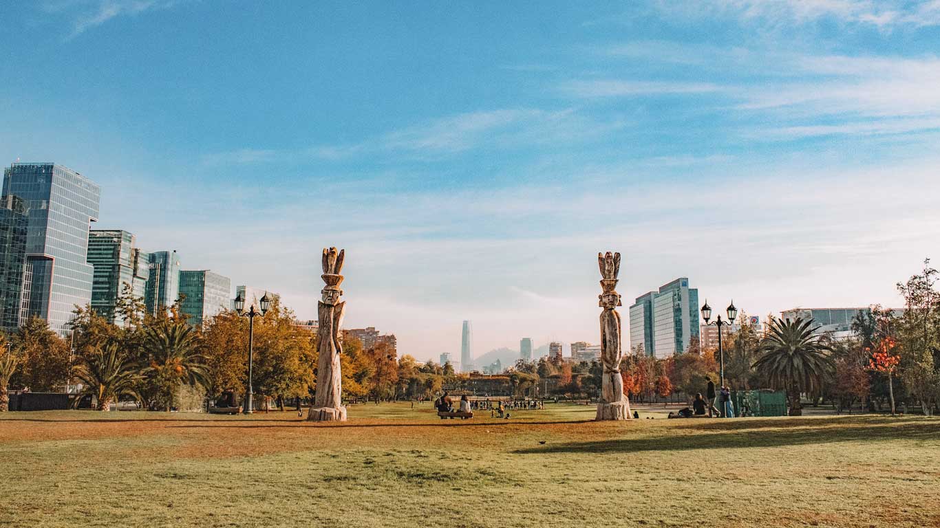 Vista do Parque em Las Condes, um bairro ideal para familias se hospedarem em Santiago, com arranha-céus modernos ao fundo e esculturas de madeira em destaque.